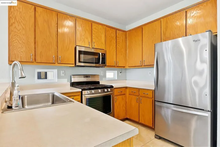 Kitchen with appliances with stainless steel finishes, brown cabinets, light countertops, and light tile patterned floors