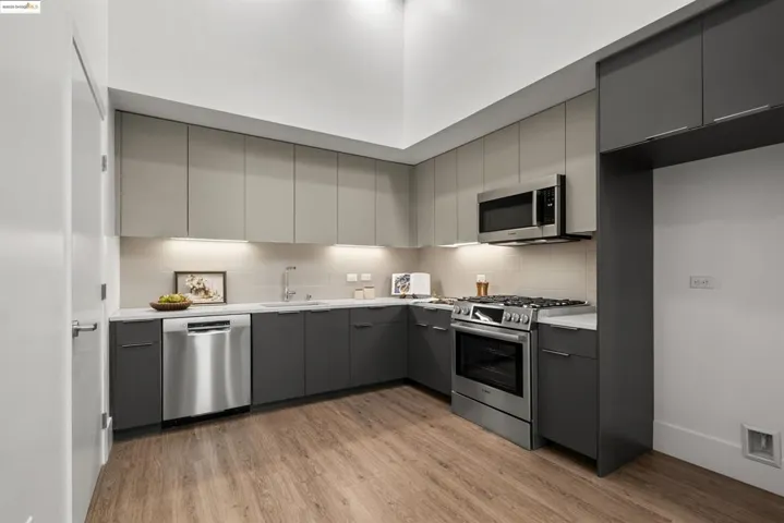Kitchen with gray cabinetry, modern cabinets, stainless steel appliances, light wood-type flooring, and tasteful backsplash