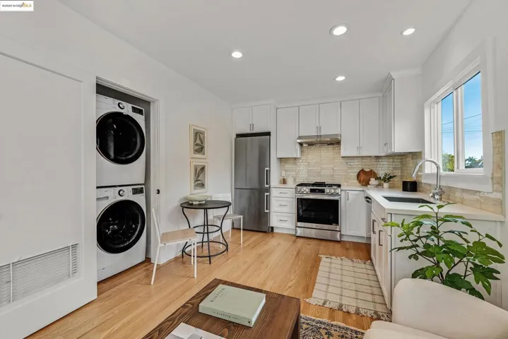 Kitchen with light wood finished floors, stainless steel appliances, white cabinetry, recessed lighting, and stacked washing machine and dryer