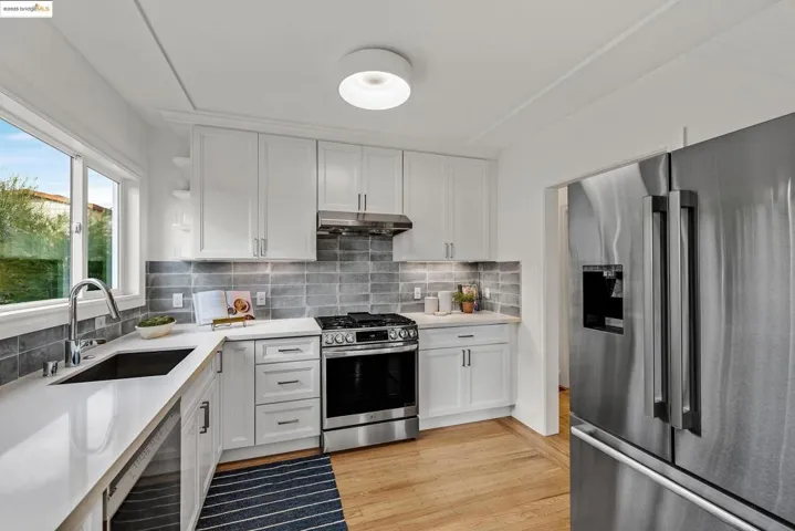 Kitchen with appliances with stainless steel finishes, white cabinetry, decorative backsplash, open shelves, and light wood-style flooring