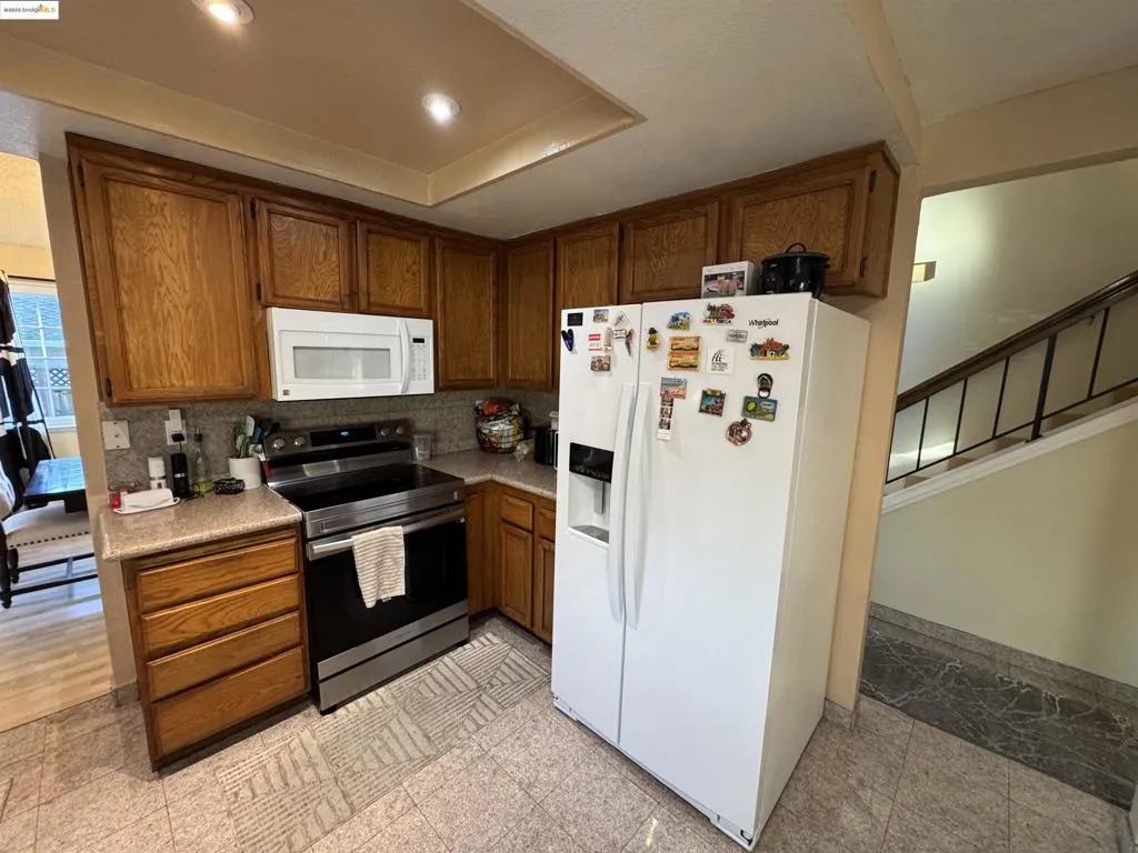 Kitchen with white appliances, brown cabinetry, granite tiled floors, decorative backsplash, and recessed lighting