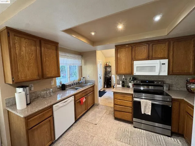 Kitchen with white appliances, brown cabinets, and recessed lighting