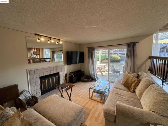 Living room featuring rail lighting, a tiled fireplace, a textured ceiling, light wood-style flooring, and plenty of natural light