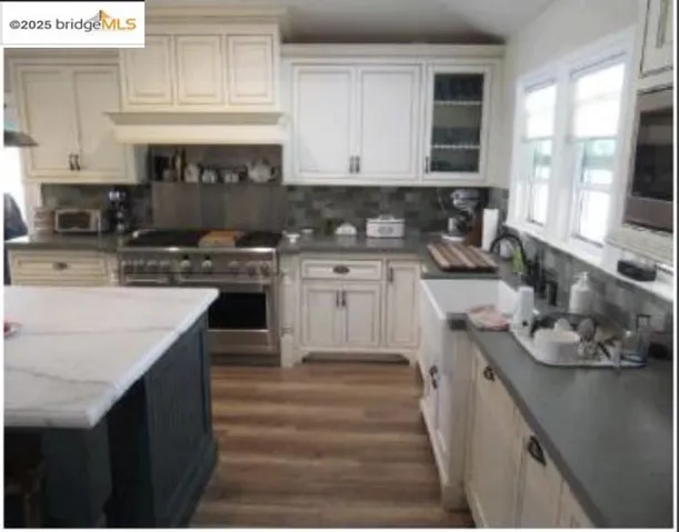 Kitchen with tasteful backsplash, stainless steel appliances, glass insert cabinets, dark wood-style floors, and extractor fan
