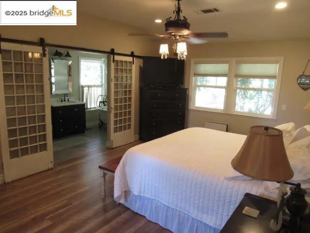 Bedroom with a barn door, dark wood finished floors, a ceiling fan, and recessed lighting