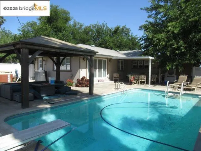 Swimming pool with a patio area, a gazebo, a diving board, and a jacuzzi