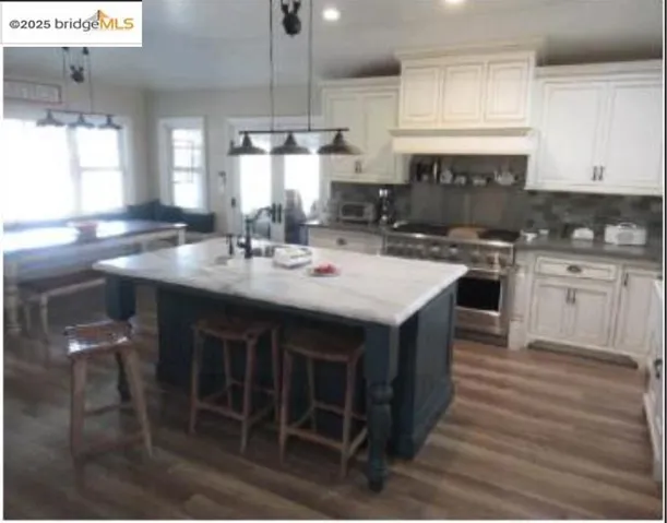 Kitchen with a breakfast bar area, hanging light fixtures, stainless steel stove, backsplash, and an island with sink