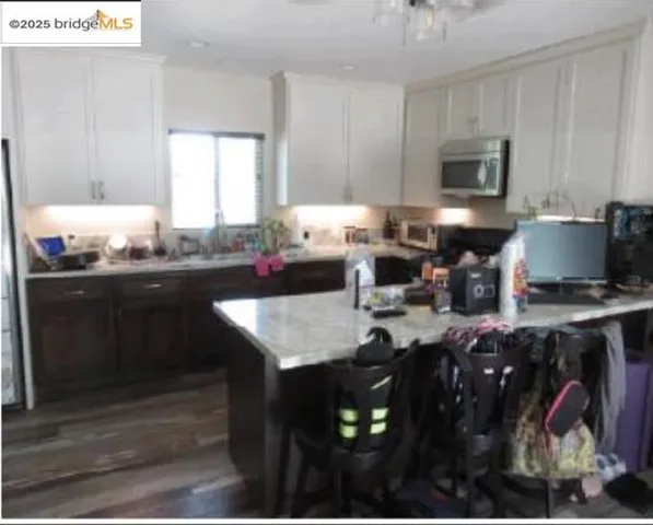 Kitchen with a breakfast bar, white cabinetry, stainless steel microwave, dark wood finished floors, and a peninsula