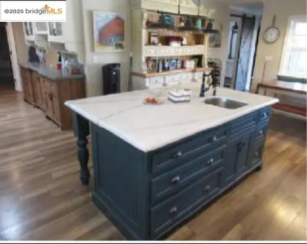 Kitchen featuring a kitchen island with sink, dark wood finished floors, glass insert cabinets, decorative light fixtures, and blue cabinets