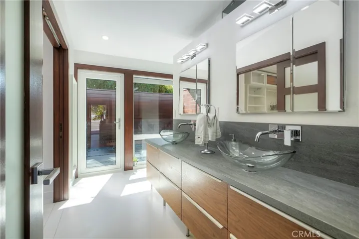 Luxurious primary bath offers private courtyard for relaxing, note the dual glass sinks,  mirrored cabinets both open to mirrored interior