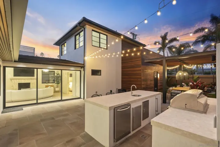 An outdoor grill pavilion with built-in stainless station, generous prep counter, and task lighting, perfect for late-summer asado under pink Pacific sunsets.