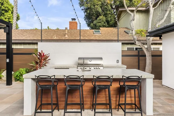 An outdoor grill pavilion with built-in stainless station, generous prep counter, and task lighting, perfect for late-summer asado under pink Pacific sunsets.