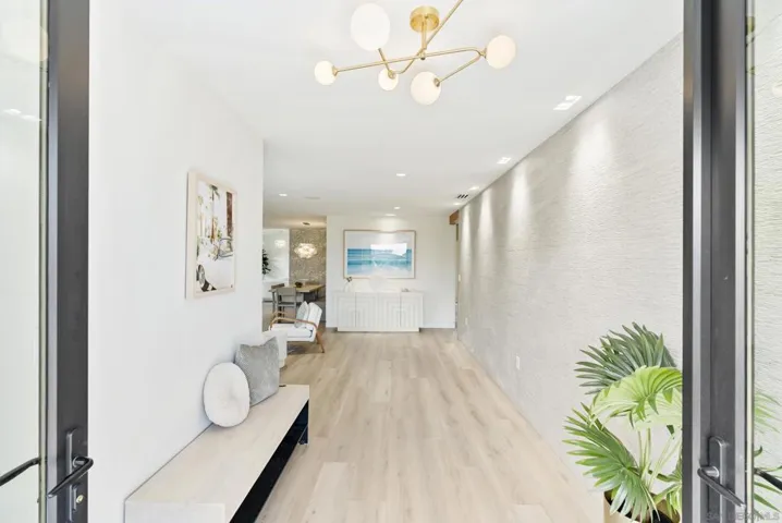 A well-lit front entrance with concealed soffit LEDs and sculpted path lights casts a warm coastal glow across glass and smooth stucco, creating a refined arrival.