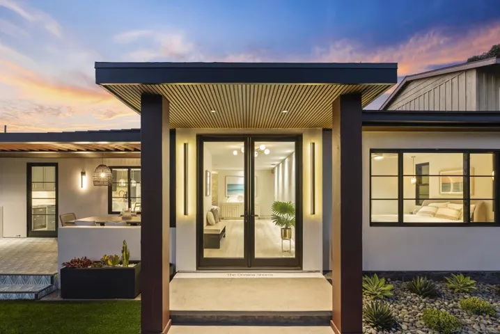 A full-height glass entry with slim black steel and minimalist hardware sets a crisp, modern welcome, flooding the foyer with soft coastal light.