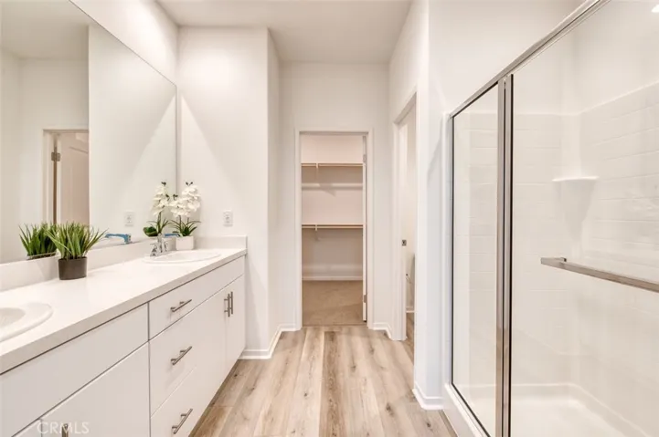 En suite primary bathroom featuring double sinks, quartz counter, white cabinetry, spacious shower, walk-in closet and privacy toilet.