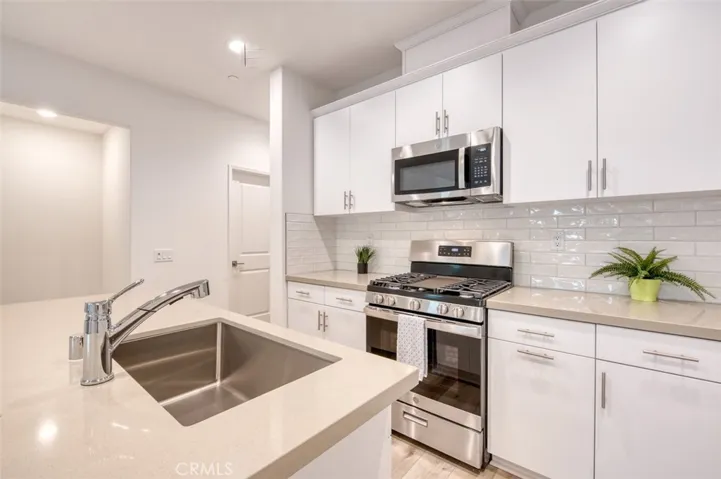 Kitchen with breakfast bar island, Stainless Steel gas range and microwave, quartz counters, white subway tile backsplash and custom​​‌​​​​‌​​‌‌​​‌​​​‌‌​​​‌​​‌‌​​‌‌​​‌‌​​​​ cabinetry.