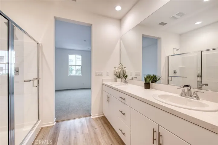 En suite primary bathroom featuring spacious shower, double sinks, quartz counter and white cabinetry.