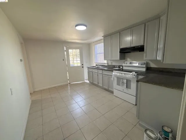 Kitchen with white electric range, light tile patterned floors, and dark stone counters