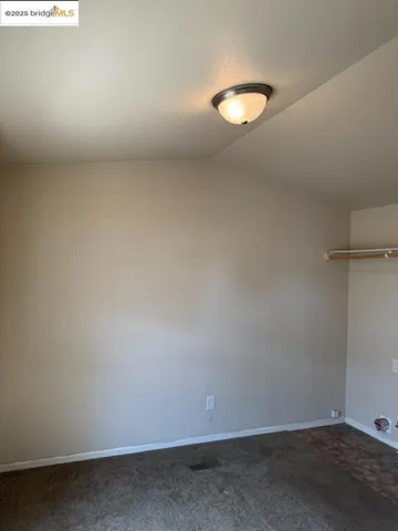 Unfurnished room featuring dark colored carpet and lofted ceiling
