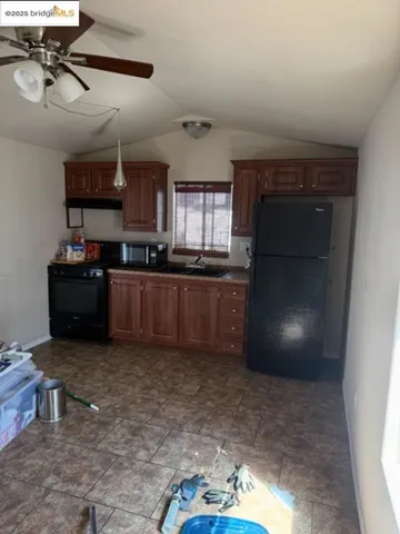 Kitchen featuring black appliances, a ceiling fan, lofted ceiling, brown cabinetry, and exhaust hood
