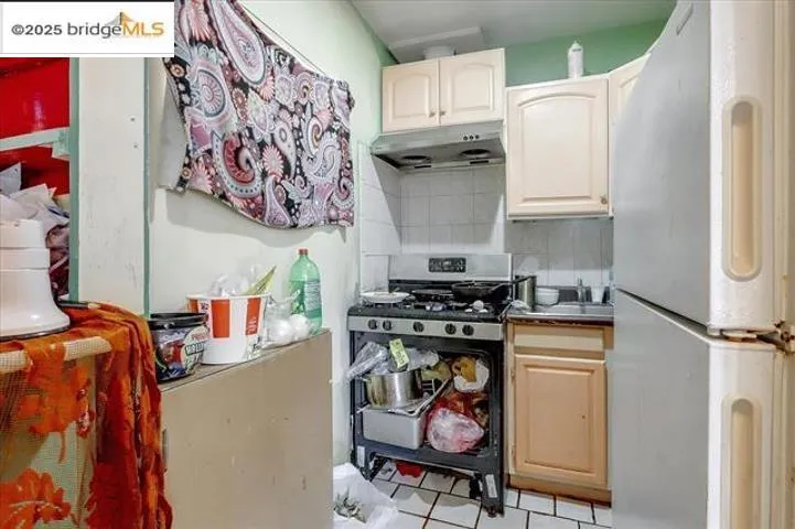 Kitchen featuring freestanding refrigerator, stainless steel range with gas stovetop, decorative backsplash, under cabinet range hood, and light tile patterned floors