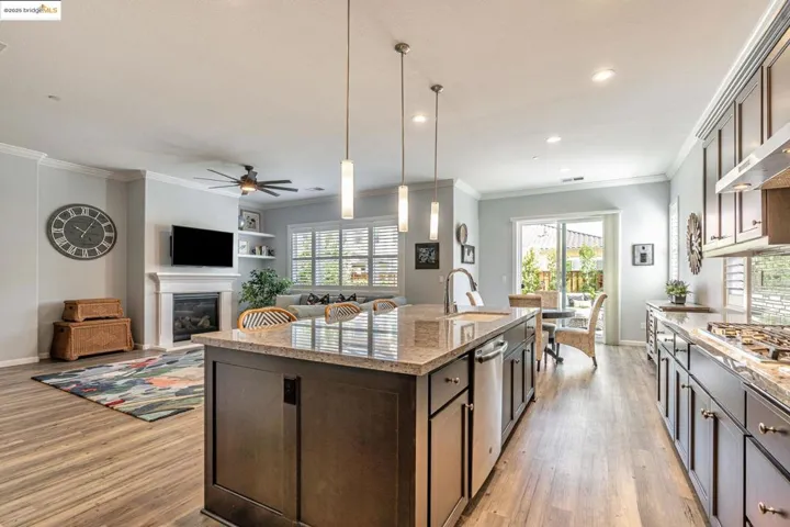 Kitchen with dark brown cabinetry, pendant lighting, light stone countertops, a center island with sink, and open floor plan