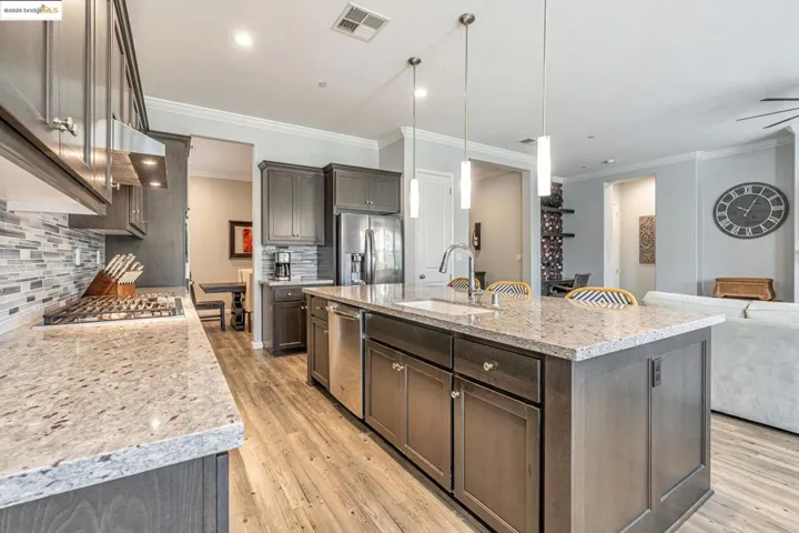 Kitchen with open floor plan, tasteful backsplash, hanging light fixtures, light stone countertops, and crown molding