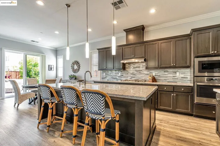 Kitchen with dark brown cabinetry, crown molding, a breakfast bar, light stone countertops, and pendant lighting