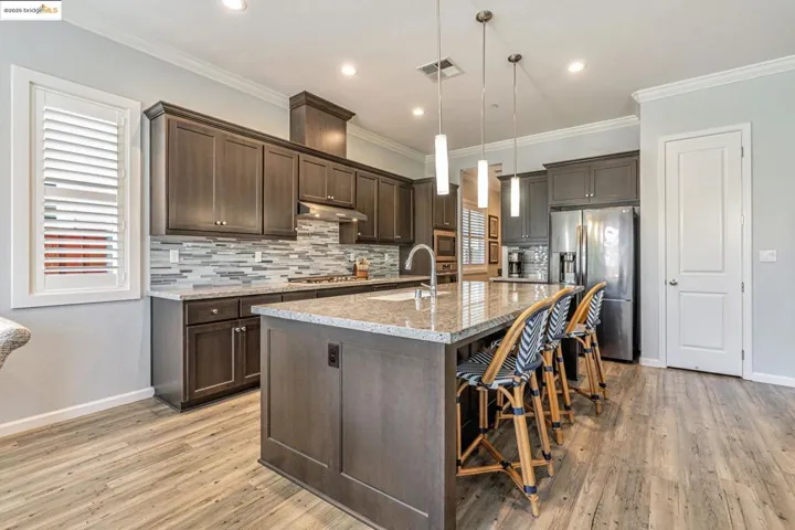 Kitchen with backsplash, light stone countertops, stainless steel appliances, a kitchen breakfast bar, and recessed lighting