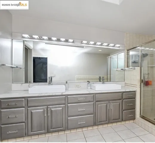 Bathroom with light tile patterned flooring, double vanity, and a stall shower