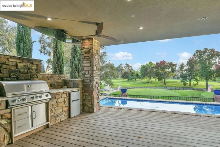 View of patio with an outdoor kitchen, an outdoor pool, a wooden deck, view of golf course, and a ceiling fan