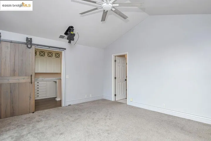 Unfurnished bedroom featuring carpet, a barn door, ceiling fan, and high vaulted ceiling