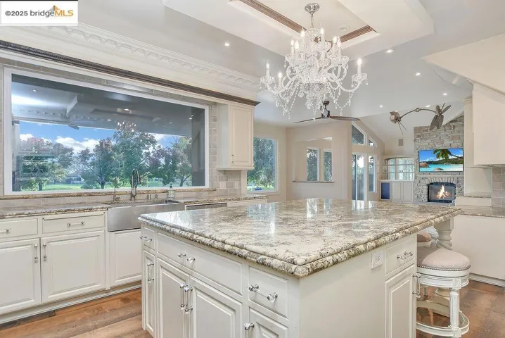 Kitchen with tasteful backsplash, a stone fireplace, light stone counters, white cabinets, and crown molding