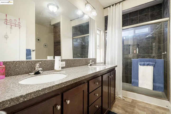 Full bathroom with double vanity, a shower stall, and light wood-type flooring