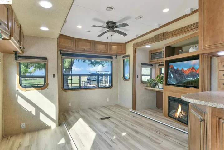 Interior space featuring brown cabinets, light wood-type flooring, recessed lighting, ceiling fan, and a glass covered fireplace