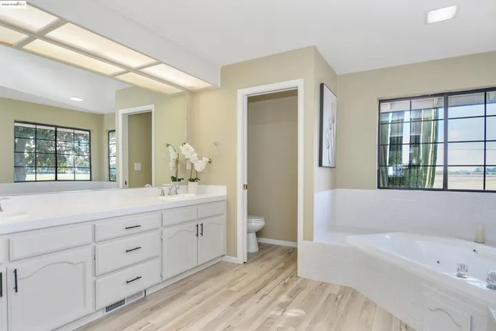 Full bathroom with double vanity, light wood finished floors, and a garden tub