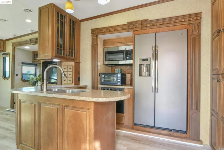 Kitchen with appliances with stainless steel finishes, brown cabinets, glass insert cabinets, light wood-style flooring, and ornamental molding