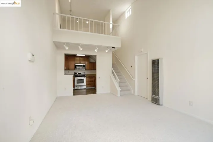 Unfurnished living room featuring rail lighting, a high ceiling, light carpet, a heating unit, and stairs