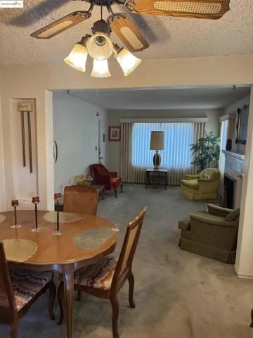 Carpeted dining area with a textured ceiling, a ceiling fan, and a fireplace