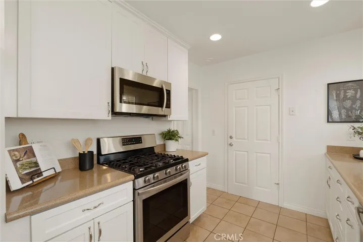Kitchen with white shaker cabinets & stainless steel appliances. Doorway to laundry room + garage