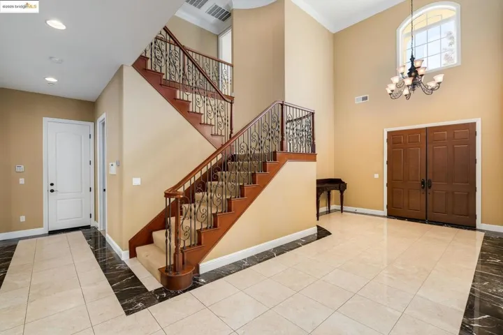 Foyer with a chandelier, tile patterned flooring, crown molding, stairs, and a towering ceiling