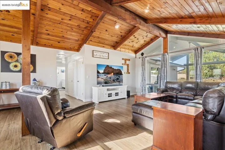 Living area with a wood ceiling with exposed beams, high vaulted ceiling, and wood finished floors