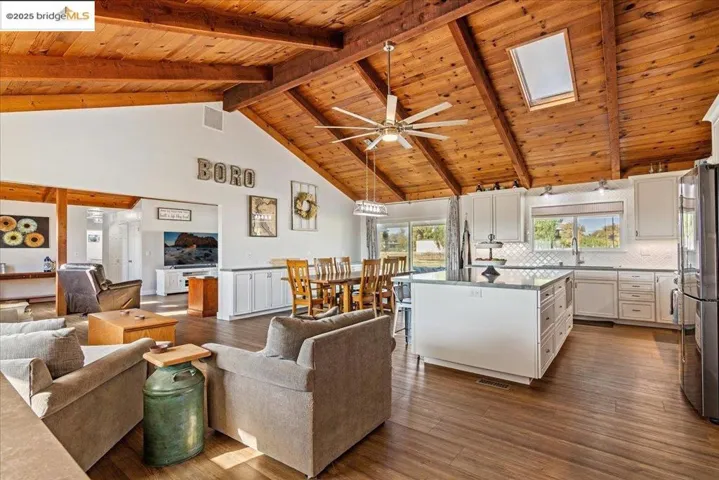 Living area with high vaulted ceiling, dark wood-style flooring, a wooden ceiling with exposed beams, and a ceiling fan