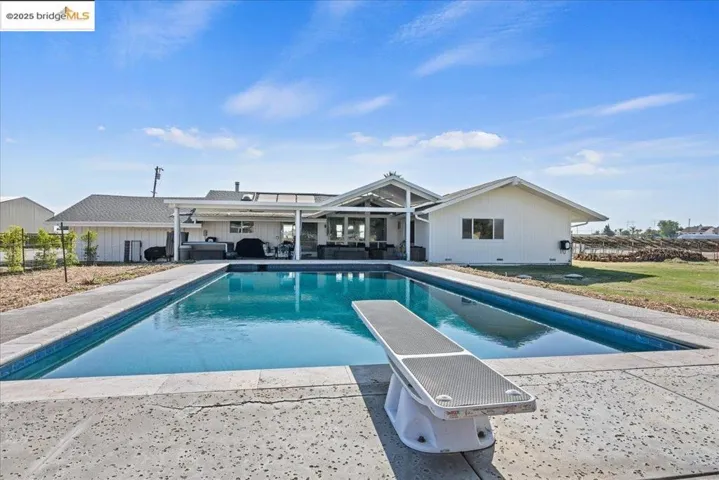 Outdoor pool with a patio area, a diving board, and outdoor lounge area