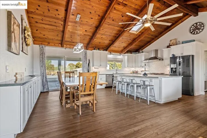 Dining space featuring high vaulted ceiling, a wood ceiling with exposed beams, dark wood-style floors, a ceiling fan, and a skylight