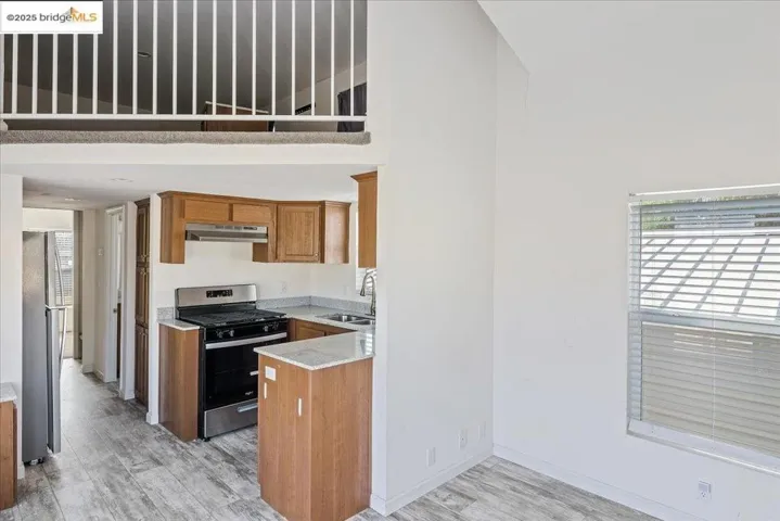 Kitchen featuring stainless steel appliances, healthy amount of natural light, light wood-style floors, brown cabinetry, and a towering ceiling