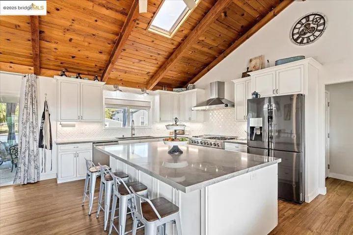 Kitchen with stainless steel appliances, a wood ceiling with exposed beams, white cabinets, a kitchen island, and backsplash