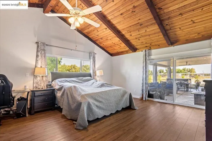 Bedroom featuring a wooden ceiling with exposed beams, high vaulted ceiling, access to exterior, wood finished floors, and multiple windows