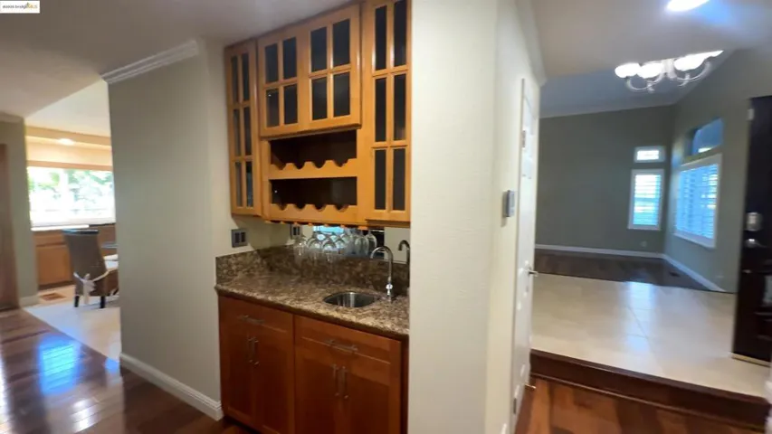 Bar area featuring open shelves, brown cabinetry, dark wood-style floors, dark stone counters, and crown molding