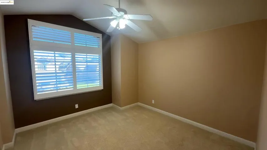 Carpeted spare room featuring a ceiling fan and vaulted ceiling